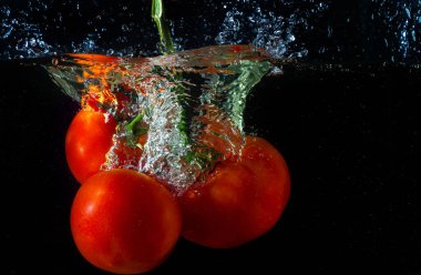 Suya düşen taze kırmızı domates. Su sıçraması ve siyah arka planda izole edilmiş hava kabarcıkları..