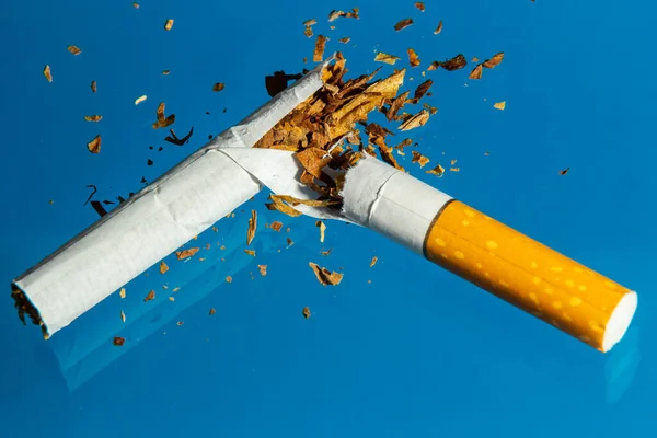 Broken cigarette on blue background. Stop smoking concept photography.