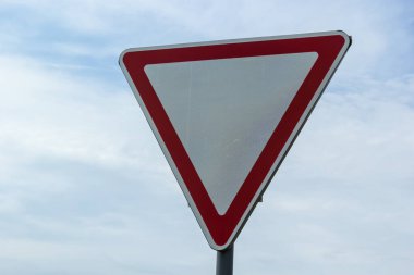 Road sign against the sky. White triangle with red border. Signal, Give way. Summer day.
