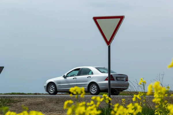 The sign Give way to the driver when exiting the highway at a rural intersection on the background of a passing car.