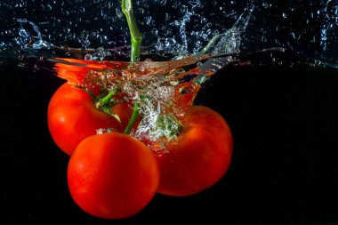 Suya düşen taze kırmızı domates. Su sıçraması ve siyah arka planda izole edilmiş hava kabarcıkları..