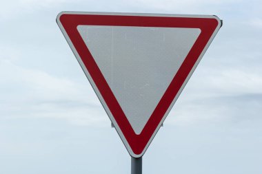 Road sign against the sky. White triangle with red border. Signal, Give way. Summer day.