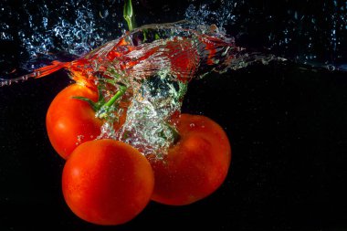 Suya düşen taze kırmızı domates. Su sıçraması ve siyah arka planda izole edilmiş hava kabarcıkları..