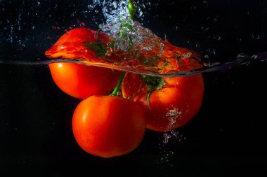 Suya düşen taze kırmızı domates. Su sıçraması ve siyah arka planda izole edilmiş hava kabarcıkları..