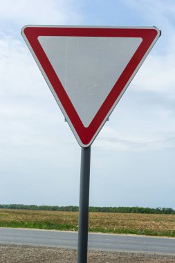 Road sign against the sky. White triangle with red border. Signal, Give way. Summer day.