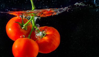 Suya düşen taze kırmızı domates. Su sıçraması ve siyah arka planda izole edilmiş hava kabarcıkları..