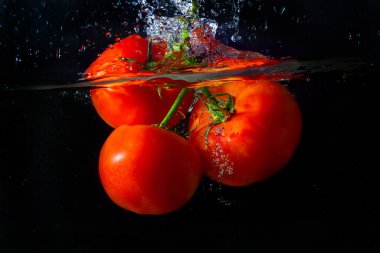 Suya düşen taze kırmızı domates. Su sıçraması ve siyah arka planda izole edilmiş hava kabarcıkları..