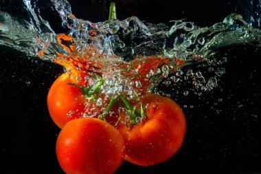 Suya düşen taze kırmızı domates. Su sıçraması ve siyah arka planda izole edilmiş hava kabarcıkları..