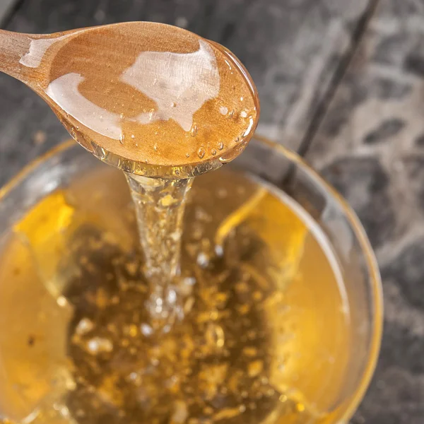 Liquid honey and wooden spoon — Stock Photo, Image