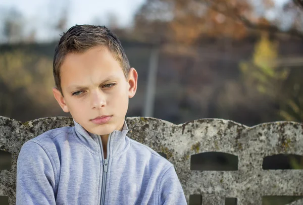 Bambino triste guardando in basso, all'aperto con una foresta in background , — Foto Stock