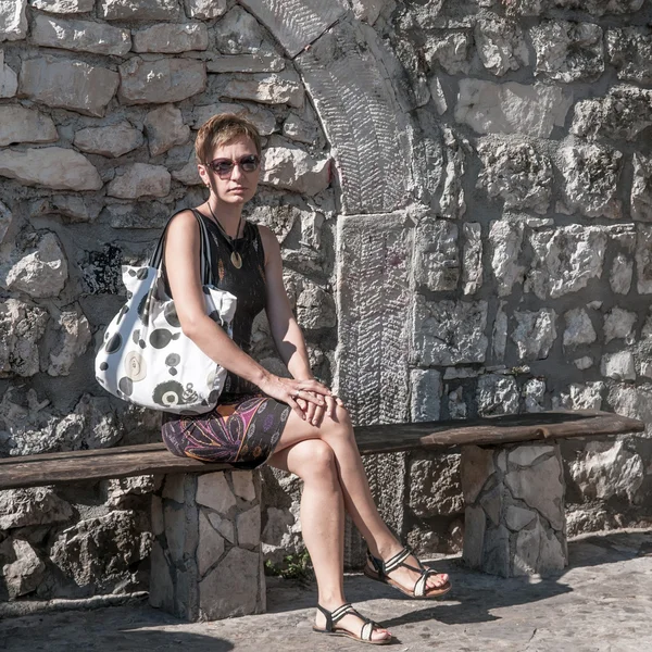 Mulher sentada na frente de uma parede de pedra velha — Fotografia de Stock