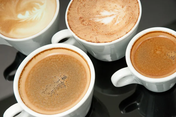 Vier witte koffie cups op de zwarte achtergrond — Stockfoto