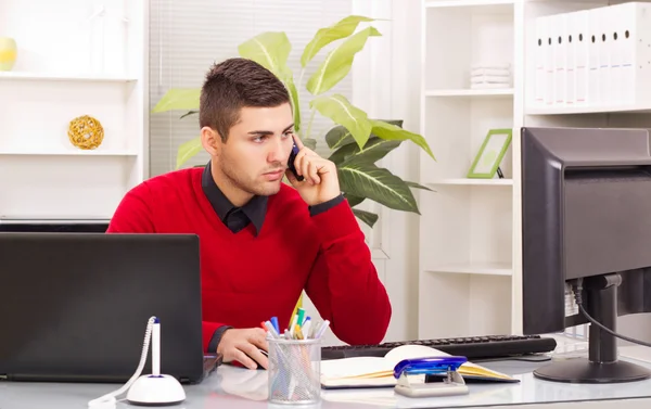 Young business man on phone while using computer at office — Stock Photo, Image