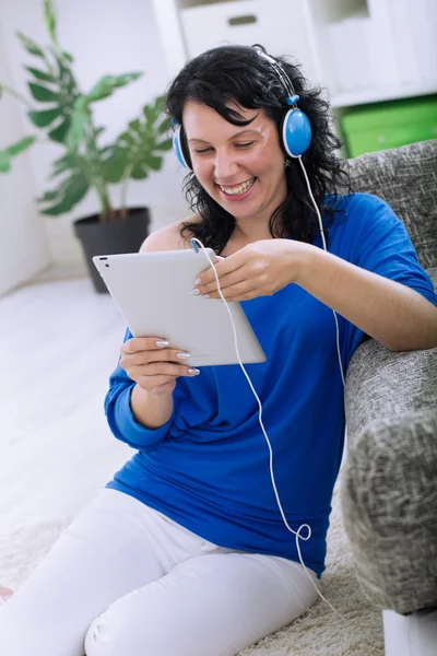 Mulher bonita com tablet e fones de ouvido em casa — Fotografia de Stock