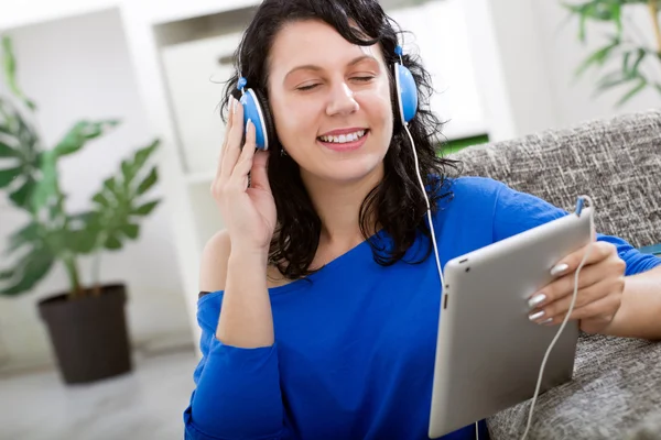Jeune femme souriante avec tablette et écouteurs à la maison — Photo