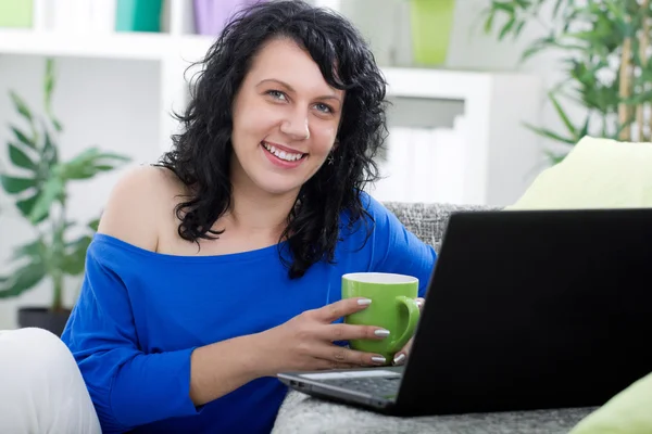 Schöne junge Frau sitzt zu Hause und trinkt Kaffee, lächelt — Stockfoto