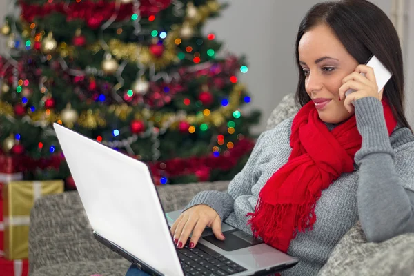 Mujeres felices usando el ordenador portátil y el teléfono celular en la noche de Navidad —  Fotos de Stock