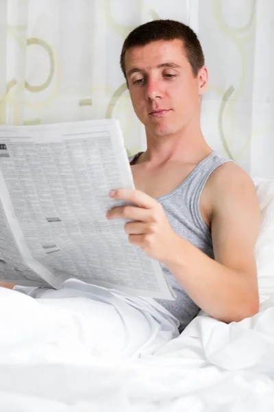 Junger Mann liest Zeitung in seinem Schlafzimmer — Stockfoto