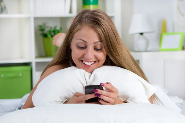 Jonge lachende vrouw kijken naar haar telefoon op het bed — Stockfoto