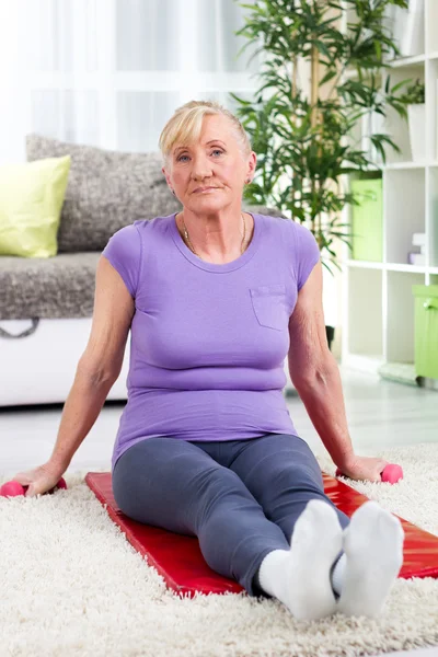 Senior woman sitting on a mat at home after training — Stock Photo, Image