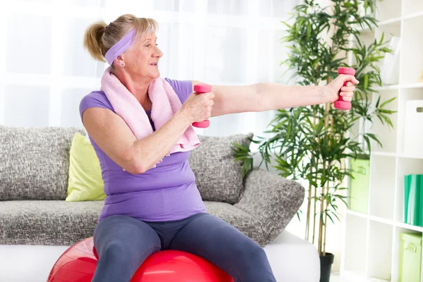 Mujer mayor feliz sentado en la pelota de gimnasio, y el ejercicio — Foto de Stock