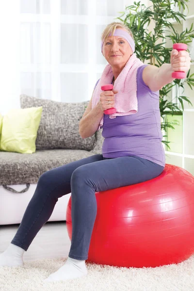 Äldre kvinna sitter på gym boll, och tränar med vikter på h — Stockfoto