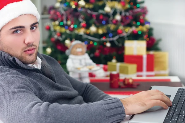 Joven hombre sonriente usando el ordenador portátil en Nochebuena — Foto de Stock