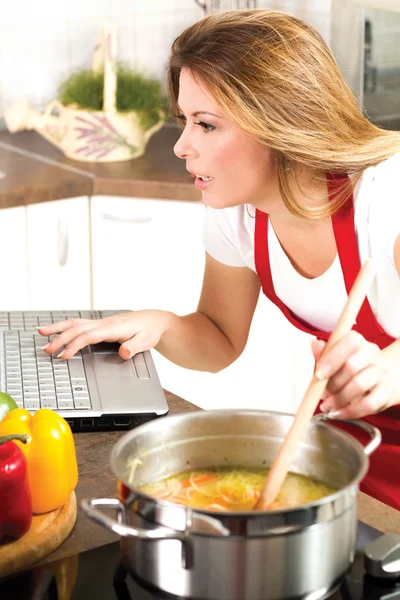 Divertido ama de casa moderna usando un ordenador portátil mientras se cocina —  Fotos de Stock