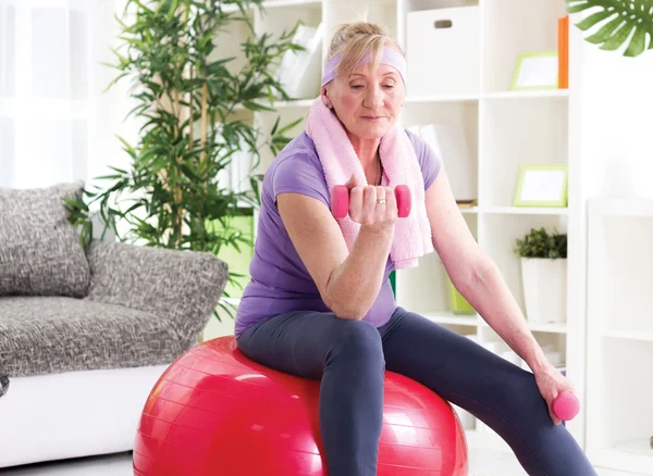 Heureuse femme âgée assise sur la balle de gymnase, et l'exercice avec l'haltère — Photo