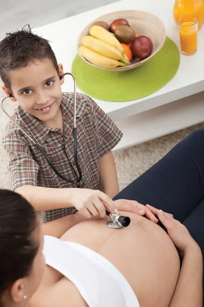 A little boy listens to a stethoscope belly of his pregnant mom — Stock Photo, Image