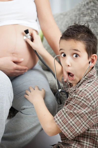 A little boy listens to a stethoscope belly of his pregnant mom — Stock Photo, Image