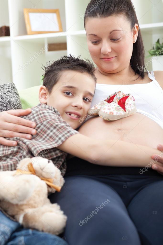 boy hugging belly of pregnant mother on sofa