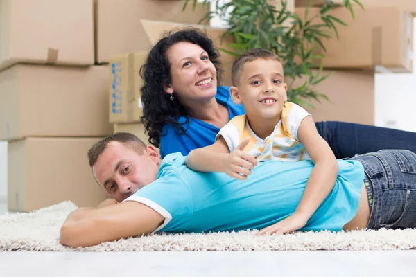 Happy couple with a kid in their new home laying on the floor — Stock Photo, Image