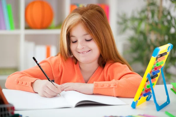 Linda niña pelirroja haciendo su tarea en casa — Foto de Stock