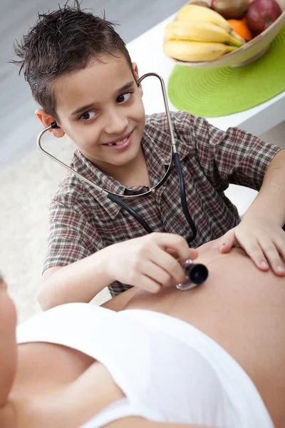 A little boy listens to a stethoscope belly of his pregnant mom — Stock Photo, Image