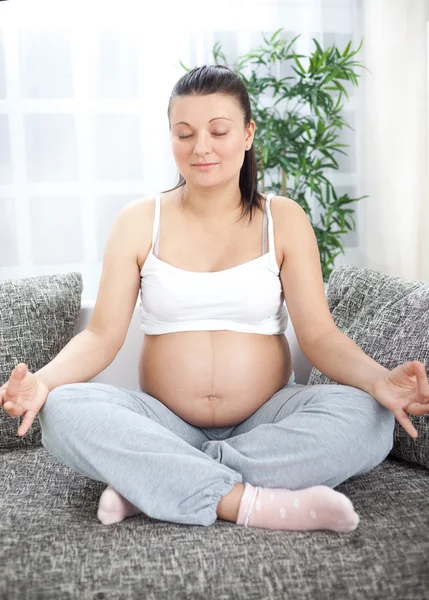 Беременная женщина расслабляется занимаясь йогой, сидя в позе лотоса, в шлюхе — стоковое фото