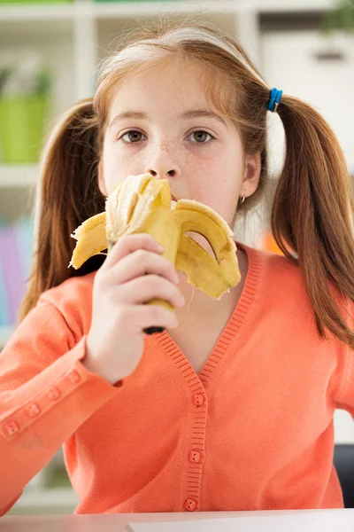 Porträtt av en vacker liten flicka äter en banan — Stockfoto
