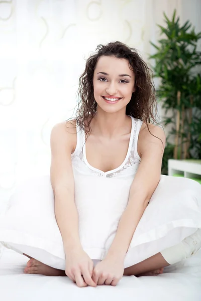 Happy young woman siting in bed in white pajamas — Stock Photo, Image