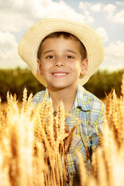 Lächelnder kleiner Junge mit Strohhut in einem Weizenfeld — Stockfoto