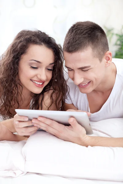 Młoda para, leżąc na łóżku, przy użyciu komputera typu tablet — Zdjęcie stockowe