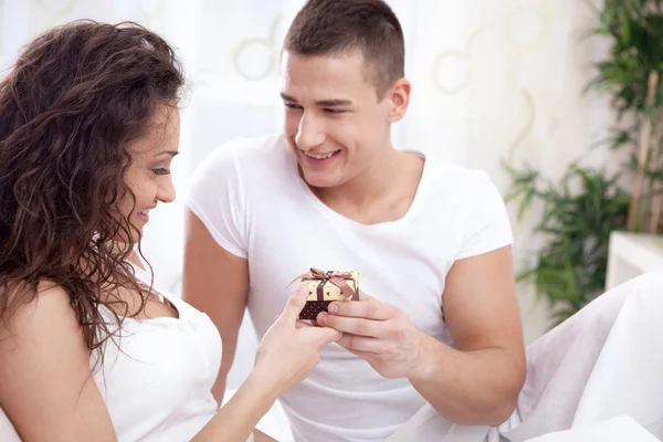 Un joven sonriente le da a una chica un regalo — Foto de Stock