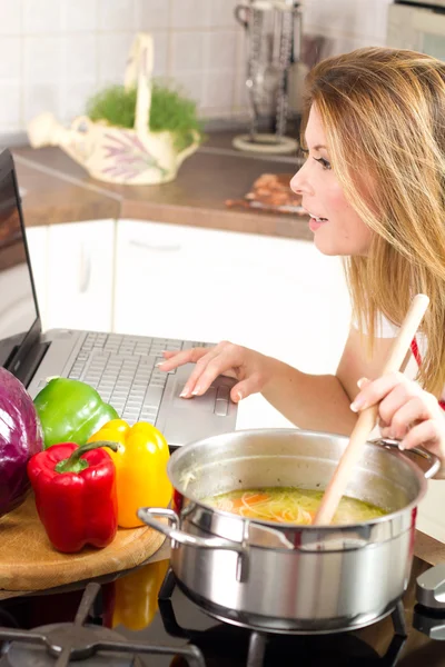 Divertente casalinga moderna utilizzando un computer portatile durante la cottura — Foto Stock