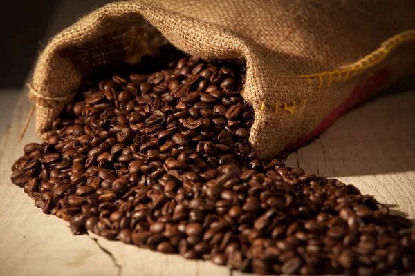 Grãos de café em saco de serapilheira contra madeira escura — Fotografia de Stock