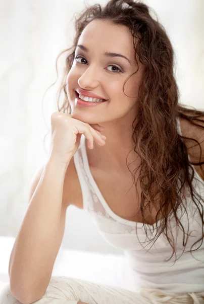 Lachende jonge vrouw die zit in de slaapkamer op het bed — Stockfoto