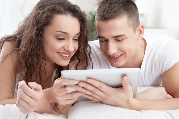 Sonriente joven pareja acostada en la cama y el uso de la tableta PC — Foto de Stock