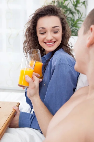 Pareja joven desayunando en la cama tostadas con zumo de naranja —  Fotos de Stock