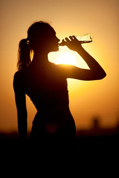 Silhouette of a young sportive woman drinking water — Stock Photo, Image