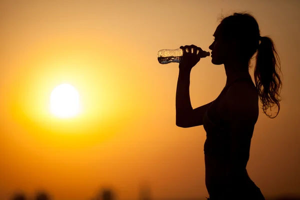 Silhouette of a young sportive woman drinking water — Stock Photo, Image