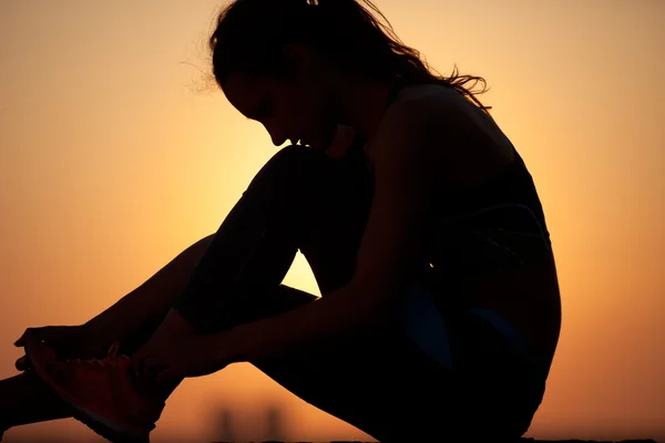 Mujer atando cordones contra el cielo amarillo al atardecer —  Fotos de Stock