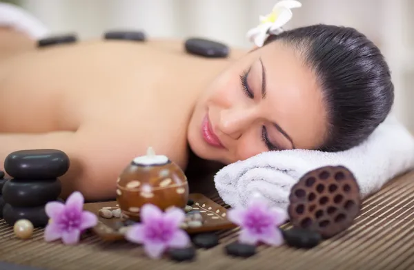 Beautiful woman in spa salon with hot stones in back — Stock Photo, Image
